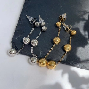 Detailed view of long ball drop earrings in polished gold and silver finishes