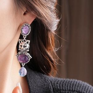 Close-up of vintage oval purple gemstone earrings with silver cat pendant on model