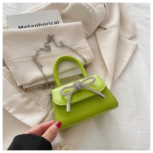 Detailed shot of neon green mini leather bag with rhinestone bow and silver chain strap