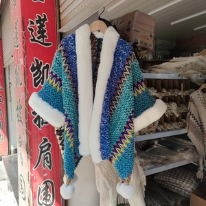 Detail of colorful zigzag knit shawl with white faux fur trim and plush ball accents