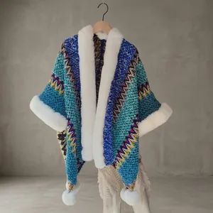 Detail of colorful zigzag knit shawl with white faux fur trim and plush ball accents