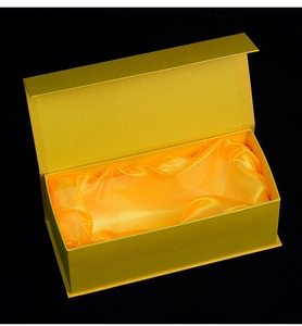 Golden rectangular gift box with pleated satin lining shown against a black background