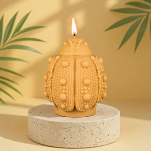 Mustard yellow beetle-shaped scented candle with textured shell on stone pedestal