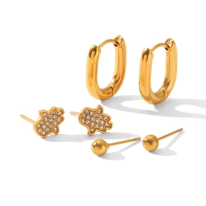 Detail of three-piece gold earring set featuring Hamsa hand with zircon and small hoops