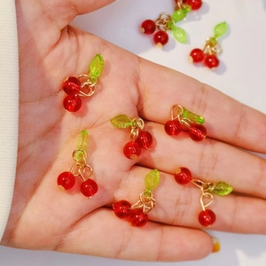 Macro shot of red cherry pendants with green leaves held in hand for scale and detail