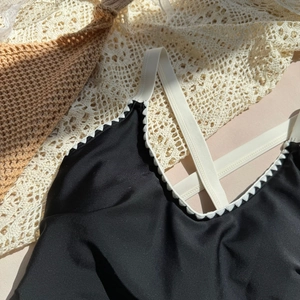 Detail of black swimsuit with white scalloped trim and thin straps on beach background