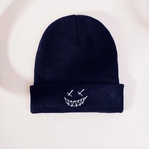 Detail of navy knit beanie featuring white embroidered cross-eyed smiley face pattern