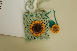 Close-up of a green hand-woven crochet bag featuring a 3D sunflower pattern and a mini charm