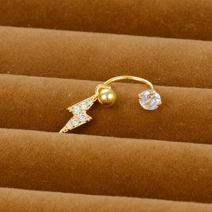 Macro detail of a gold lightning bolt belly ring with inlaid zircons on brown velvet