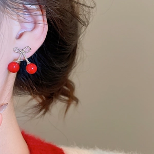 Detail of red cherry earrings with bow, showing size and fit on model's ear