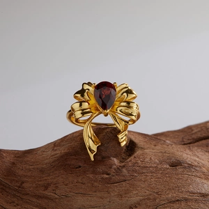 Macro shot of a gold bow ring featuring a red pear-cut gemstone on a wooden stand