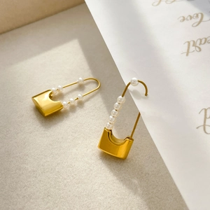 Detailed shot of golden padlock and pearl drop earrings on a minimalist background