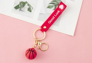 Detail of red and black basketball keychain with Good Luck leather strap and gold clasp