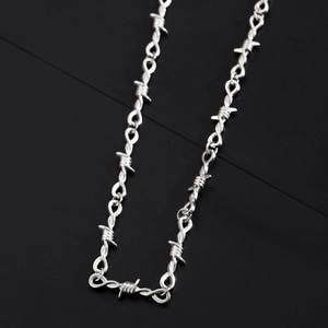 Detailed view of silver barbed wire chain necklace on a reflective black background