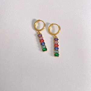 Close-up of gold drop earrings with multi-colored zirconia stones on white leather