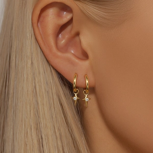 Detailed view of gold star hoop earrings with white zircon on female model ear