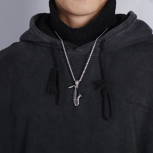 Close-up of a silver saxophone pendant necklace on a black hoodie for men