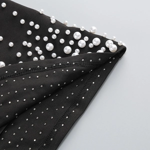 Détail macro du tissu noir de la robe avec perles blanches et strass argentés brillants