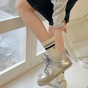 Detail of silver metallic sneakers with off-white mid-calf socks featuring smile patterns