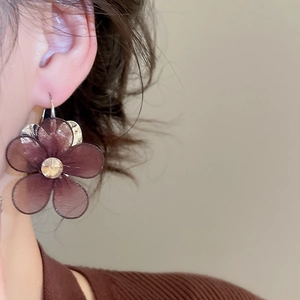 Detailed view of dark brown mesh flower earring with rhinestone center on model