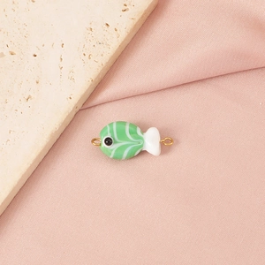 Macro detail of handmade green and white glass fish bead with gold rings for DIY jewelry