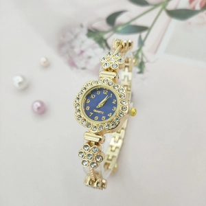 Close-up of a floral rhinestone bezel on a gold metal watch with a navy blue dial