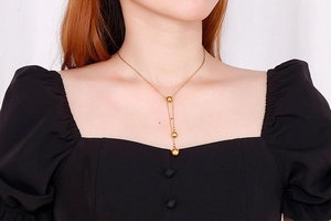 Detail of a gold drop necklace with three steel beads worn by a model on a black top