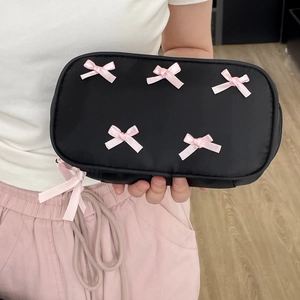 Close-up of black makeup bag with pink bows held by hands over a wooden floor
