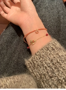 Macro detail of 18k gold-plated pony bracelet with red beads and coin charm on wrist
