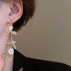 Close-up of elegant gold petal tassel earrings with pearls on model in soft lighting