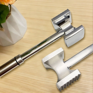 Dual-sided stainless steel meat mallet for tenderizing steak on a wooden surface