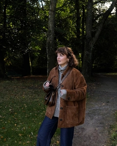 Détail de la veste en daim marron avec col roulé gris et sac bandoulière en cuir