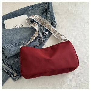 Detail of burgundy nylon crossbody bag with geometric pattern wide strap on denim