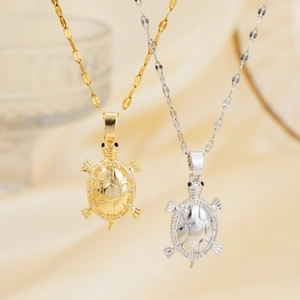 Close-up of gold and silver turtle pendants with white zircon inlay on silk background