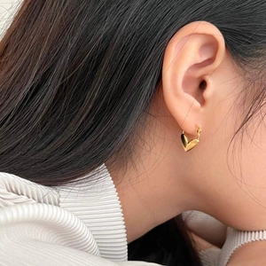 Close-up detail of a woman wearing gold heart-shaped hoop earrings with polished finish