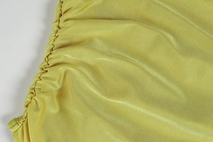 Detail of yellow ruched knit fabric texture and high-quality stitching on a summer dress