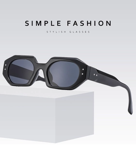 Detail of chunky black geometric sunglasses with metal rivets on white minimalist cubes