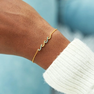 Detail of wave-shaped 18K gold bracelet with inlaid blue gems on a model's wrist