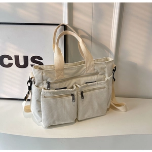 Detailed view of off-white corduroy tote bag with dual front zip pockets and adjustable strap