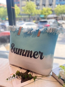 Details der blau-weißen Strandtasche aus Geflecht mit Fransen und Summer-Schriftzug
