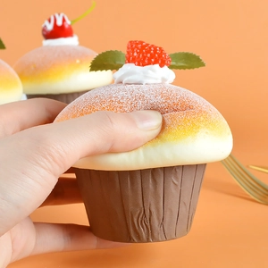 Hand squeezing a realistic PU artificial muffin cupcake with berries on orange background