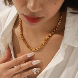 Detail shot of an 18K gold plated braided chain necklace worn on a neck with a white shirt