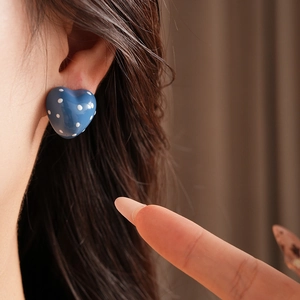 Close-up of a model wearing blue heart-shaped earrings with white polka dots