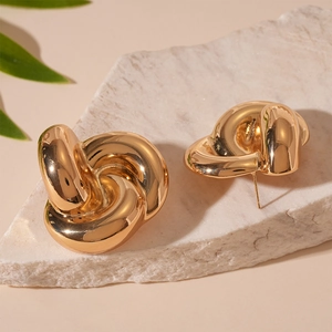 Close-up of golden knot earrings on textured stone base with artistic lighting