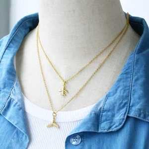 Close-up of double-layer gold necklace featuring airplane and crystal mermaid tail pendants