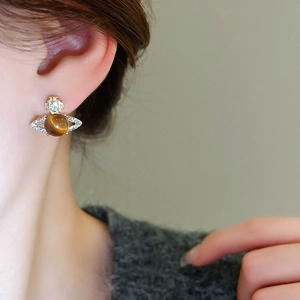Close-up of golden Saturn planet stud earrings with brown gemstone and white rhinestones