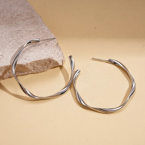 Minimalist silver geometric twisted hoop earrings displayed on a natural stone background