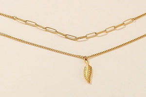 Detail of a double-layered gold wing necklace with a paperclip chain and feather pendant