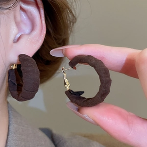 Detail of dark brown fabric wrapped C-shaped hoop earrings with gold-tone metal studs