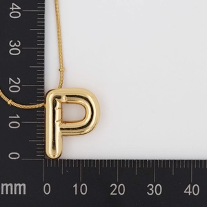 Macro detail of puffy 3D golden letter P pendant necklace next to a measuring ruler